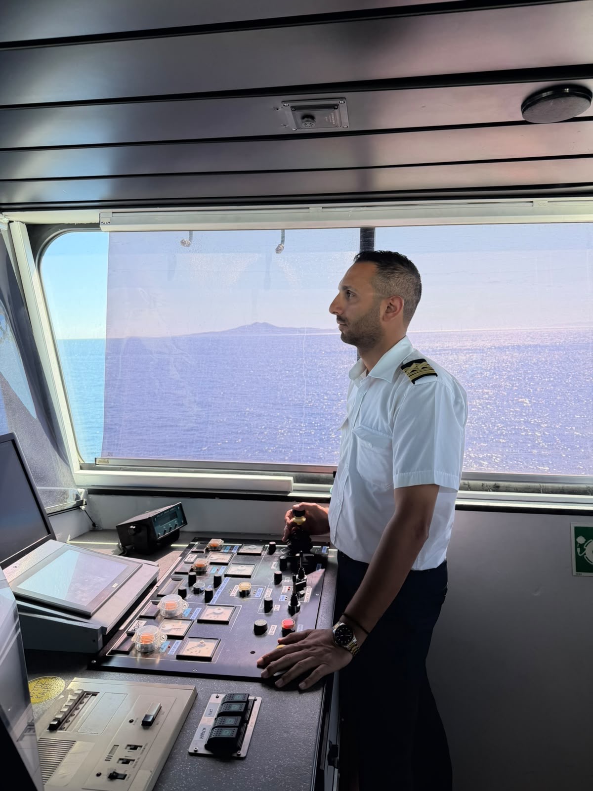 Officer on a vessel bridge beside navigational controls
